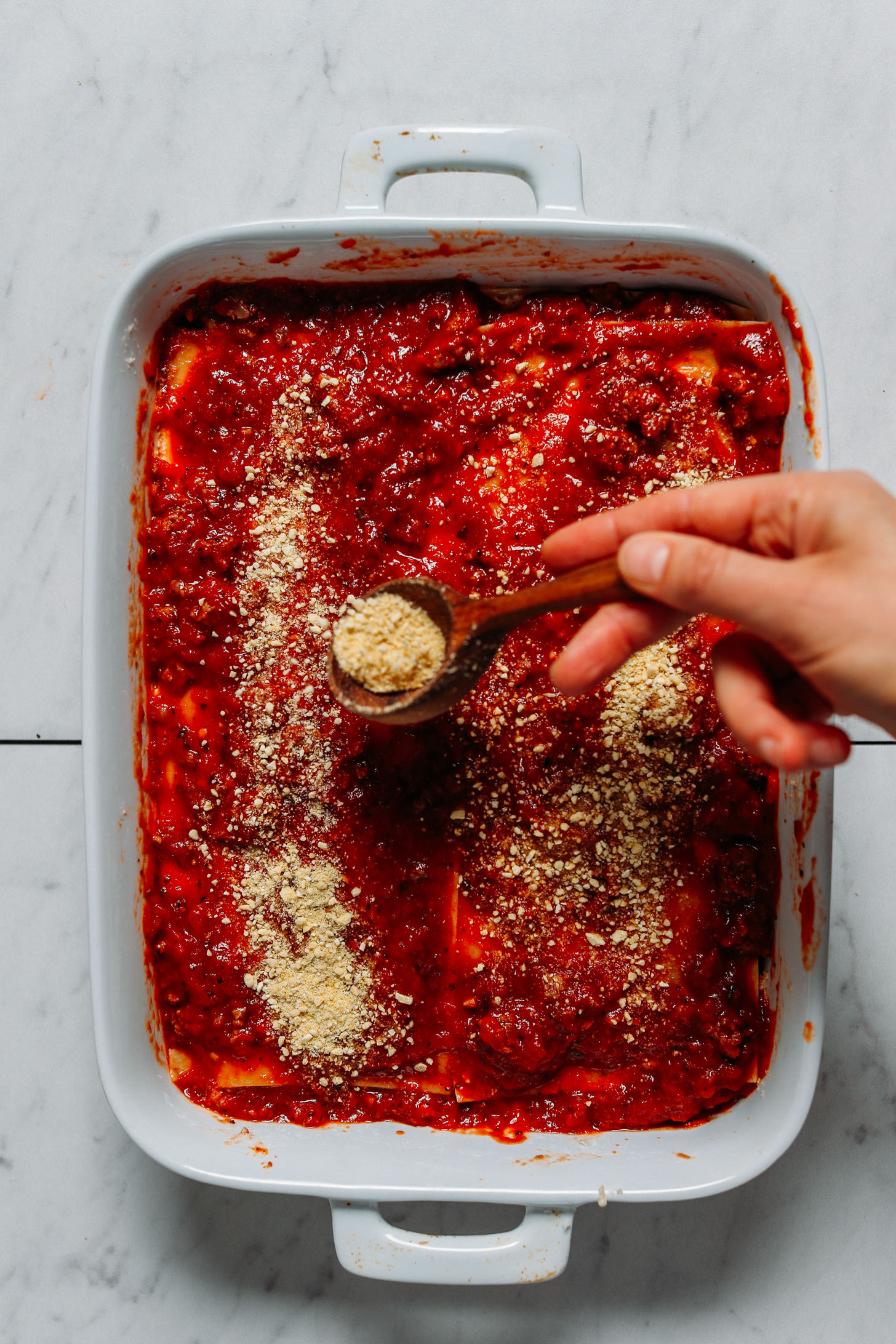 Sprinkling vegan parmesan cheese onto a pan of our gluten free lasagna