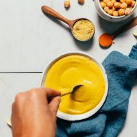 Using a spoon to stir a bowl of Liquid Gold Sauce inspired by The Whole Bowl's Thali Sauce