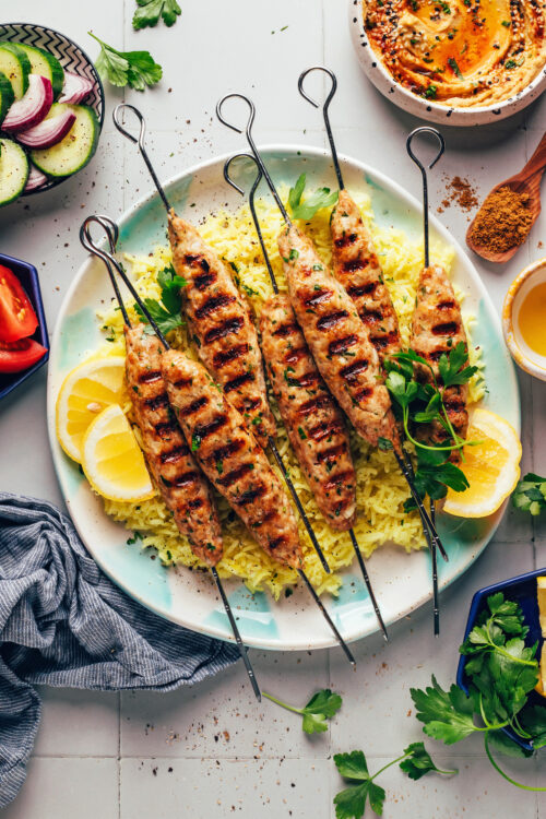 Chicken kofta kebabs on a plate over lemon rice with other items around it for serving