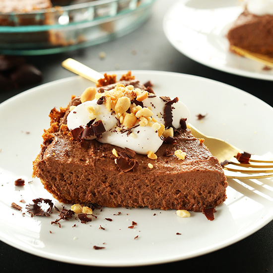 Plate with a slice of Chocolate PB Mousse Pie topped with coconut whipped cream, shaved chocolate, and peanuts