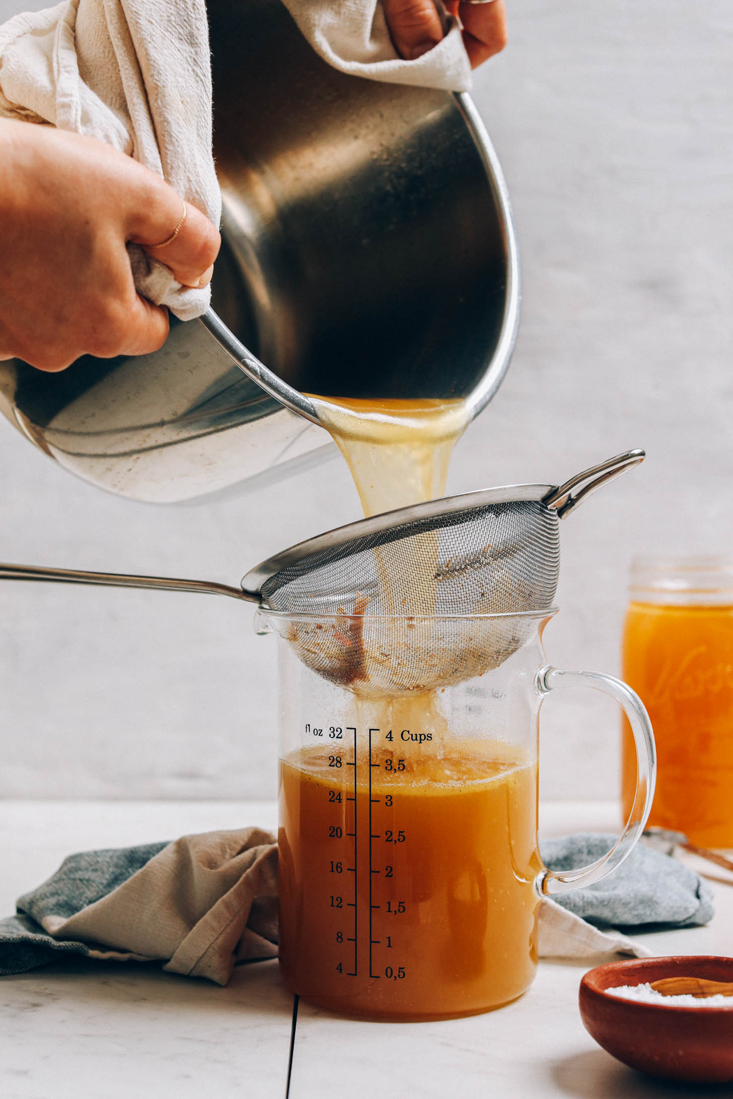 Pouring chicken stock through a fine mesh strainer into a measuring glass