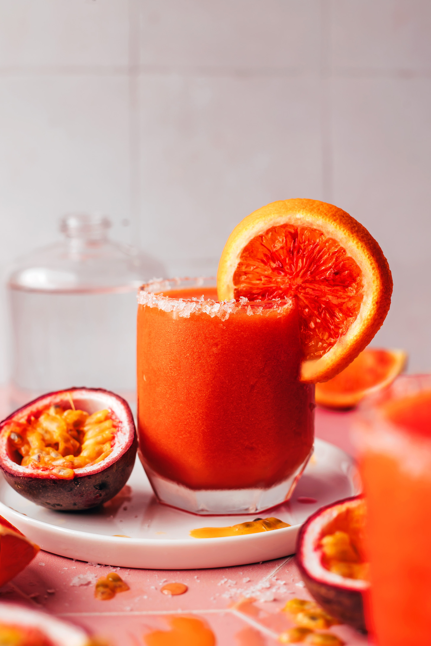 Slice of blood orange on the rim of a glass of our frozen passion fruit mezcalita with fresh passion fruit next to it