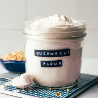 Jar of homemade buckwheat flour next to a bowl of buckwheat groats used to make it