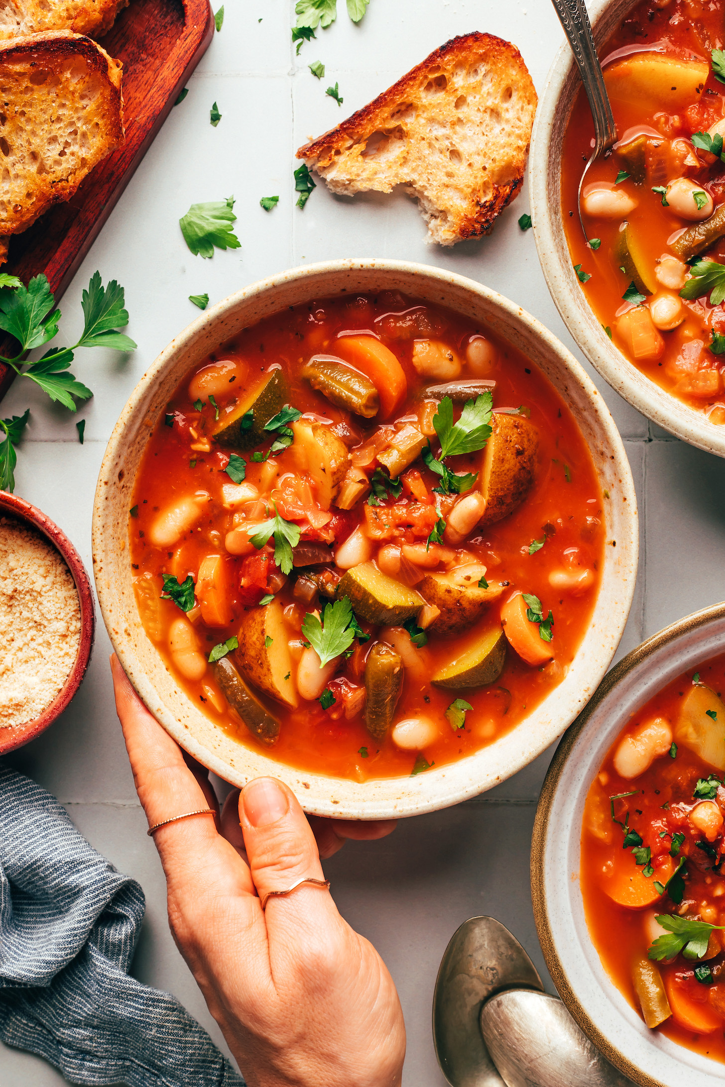 Hand holding the side of a bowl of veggie white bean minestrone soup