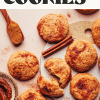 Vegan and gluten-free apple butter snickerdoodle cookies next to cinnamon sticks, ground cinnamon, and apple butter