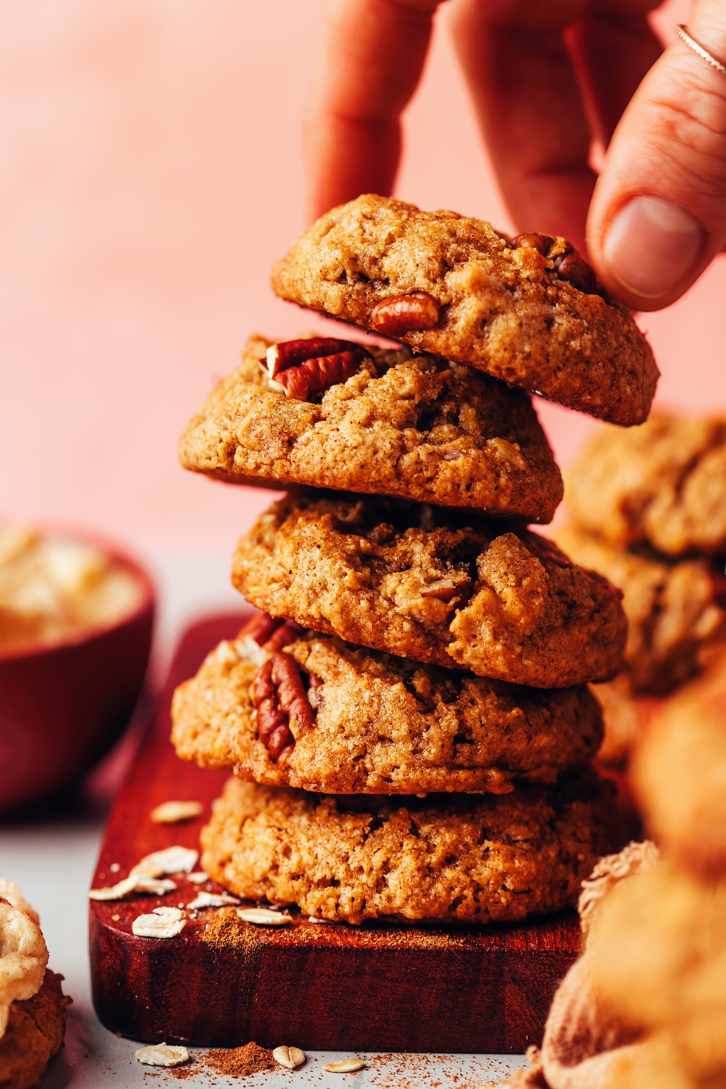 Picking up a fluffy vegan gluten-free pumpkin oat cookie from a stack of cookies