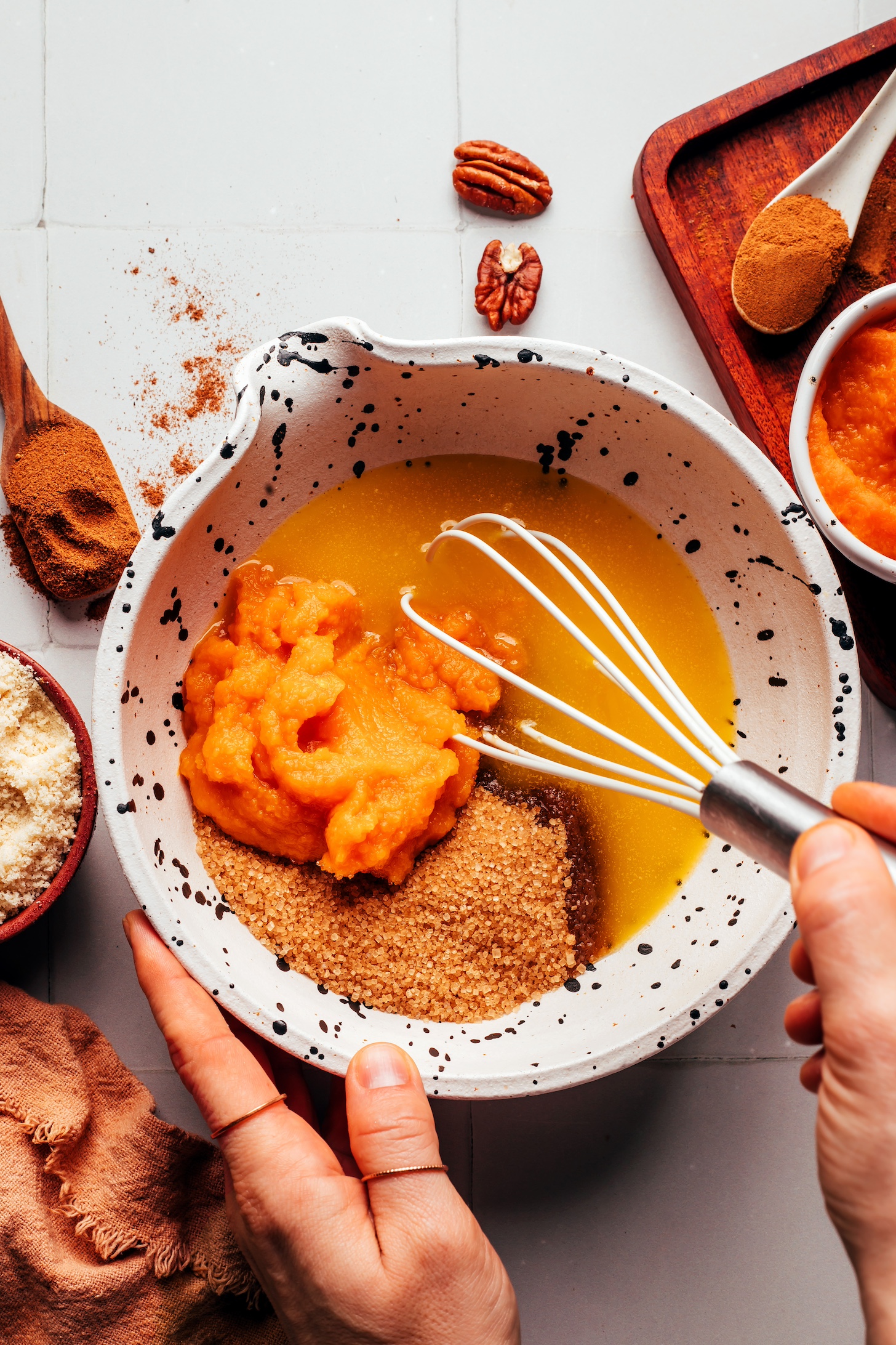 Using a whisk to combine melted vegan butter, pumpkin purée, and brown sugar