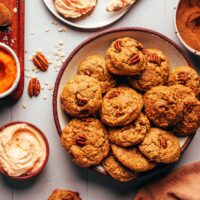 Plates of unfrosted and frosted pumpkin oat cookies next to ingredients used to make them