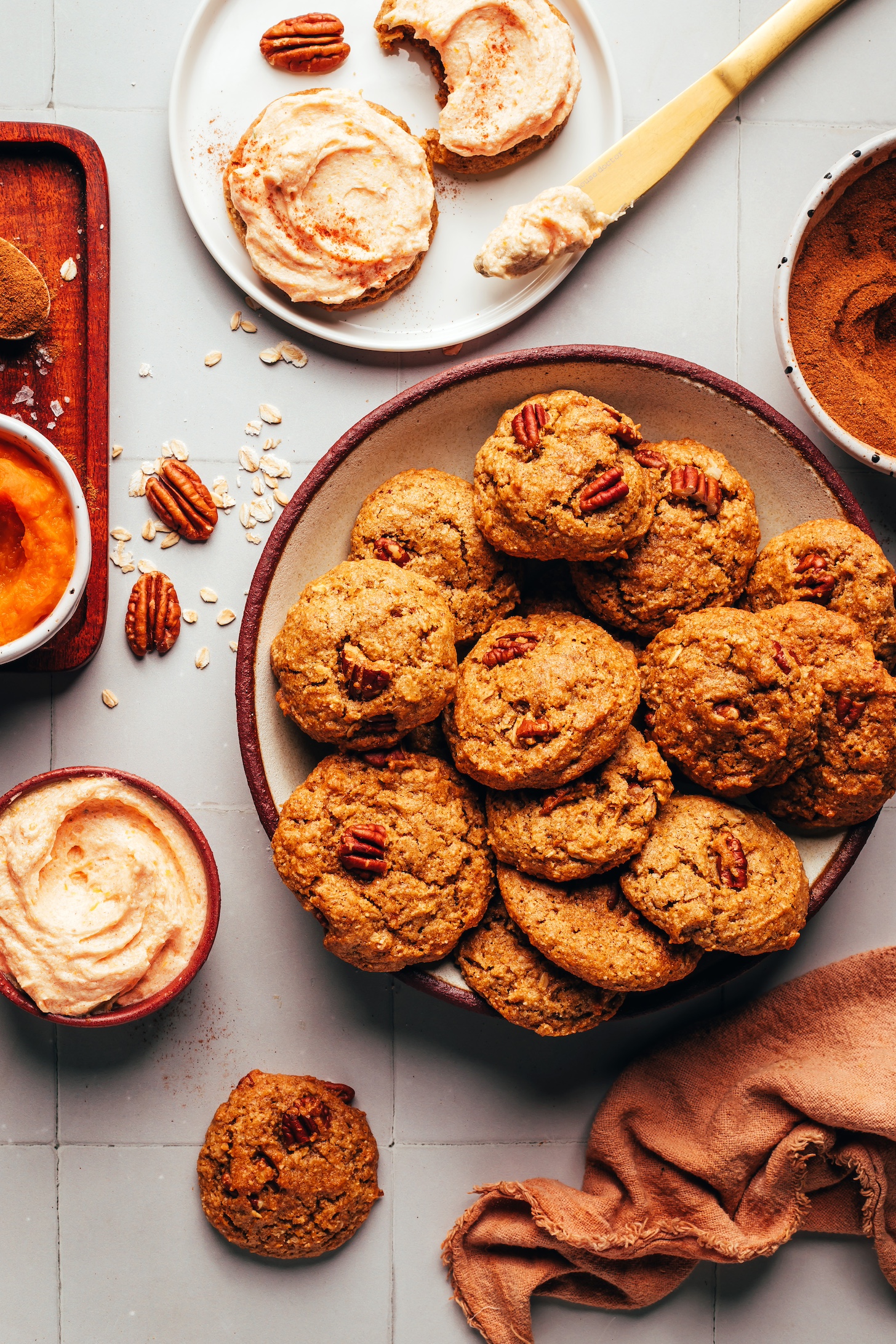 Bowl of fluffy pumpkin oat cookies next to a plate of frosted cookies and ingredients used to make the cookies