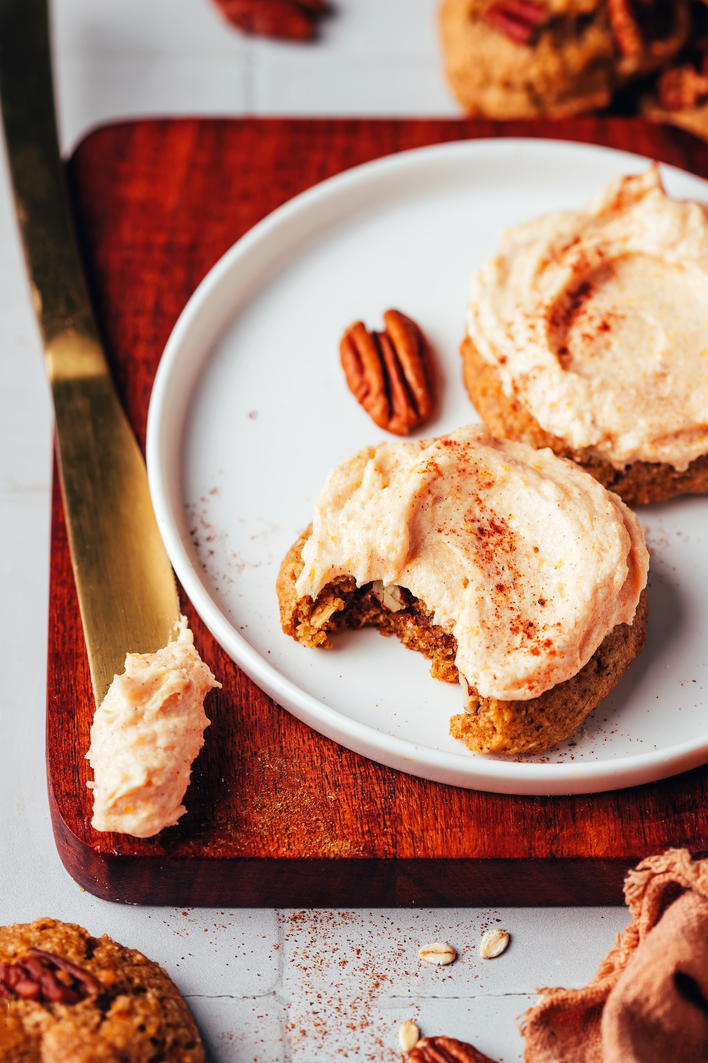 Plate of frosted pumpkin oat cookies next to a knife with pumpkin spice frosting