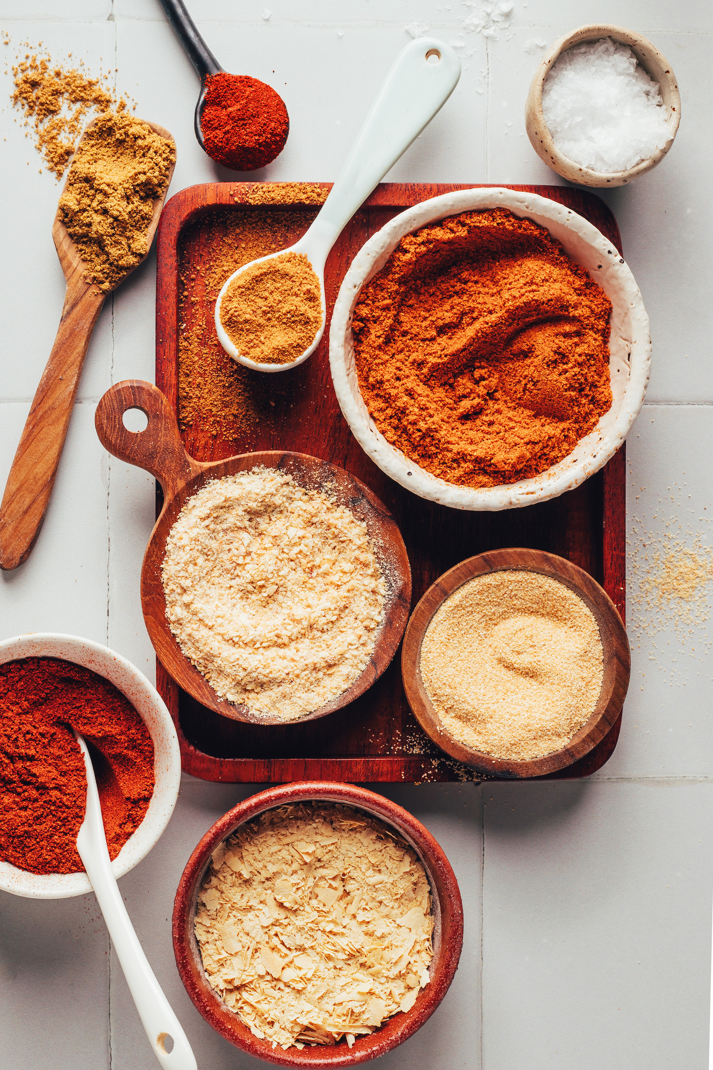 Bowls of nutritional yeast, smoked paprika, onion powder, garlic powder, chili powder, coconut sugar, cumin, chipotle powder, and salt