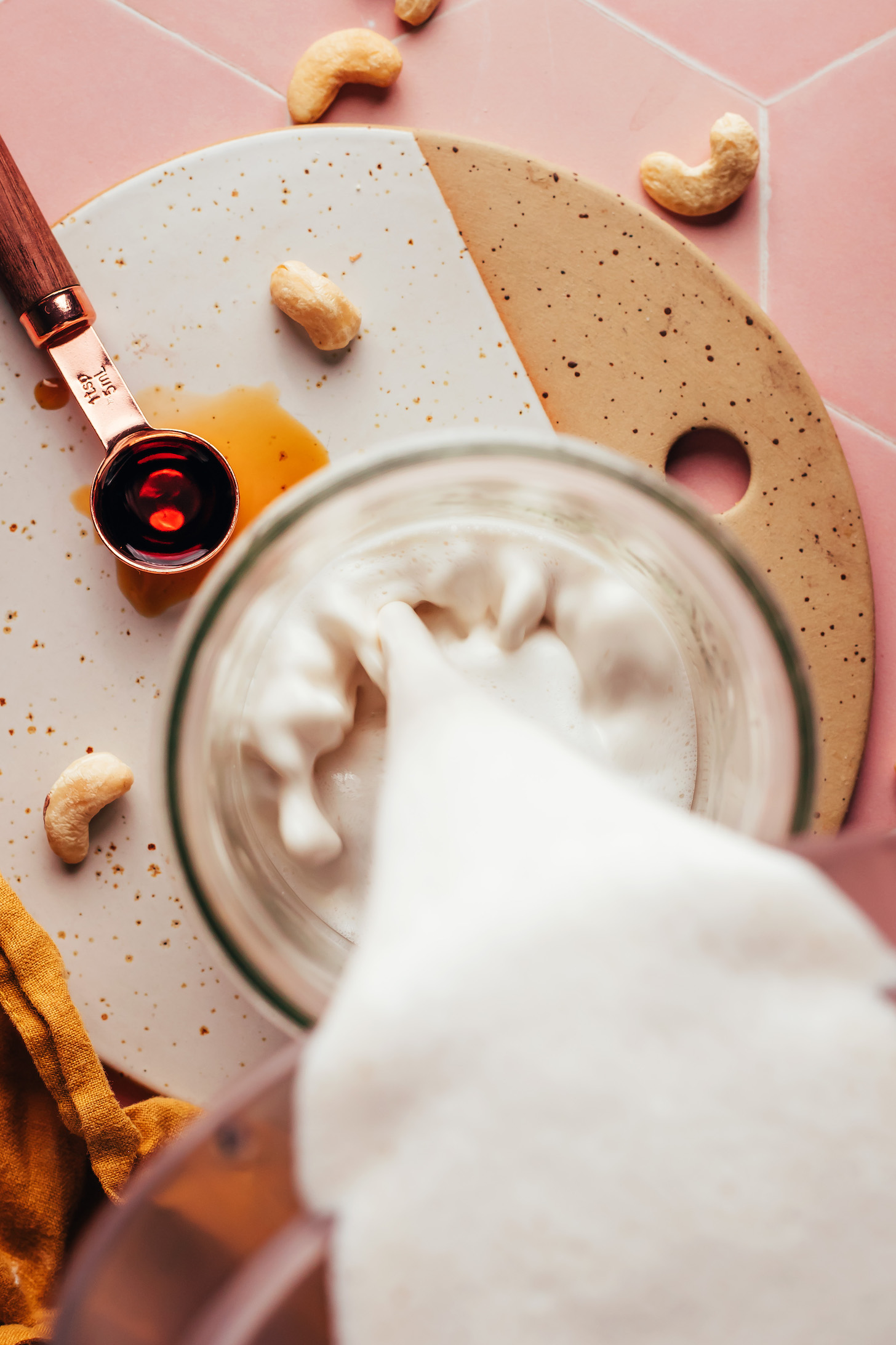 Pouring a creamy cashew mixture into a glass jar