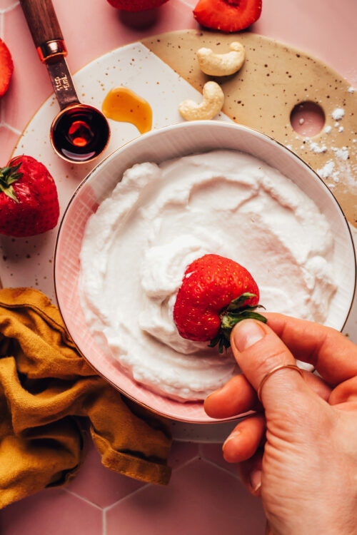 Dipping a fresh strawberry into a bowl of vegan cashew whipped cream