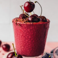 Placing a fresh cherry on the top of a chocolate cherry protein smoothie