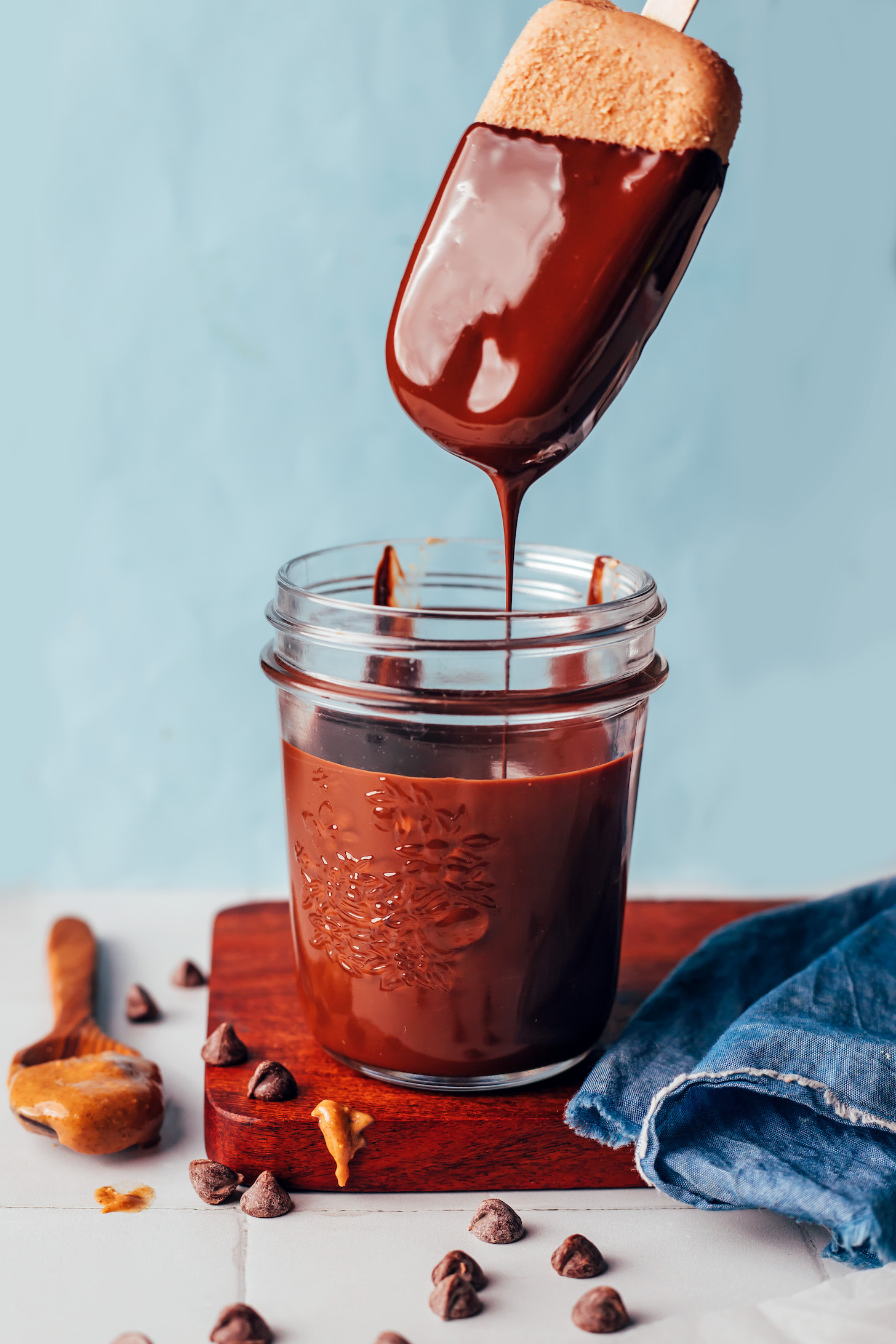 Chocolate-dipped ice cream bar dripping into a jar of melted chocolate