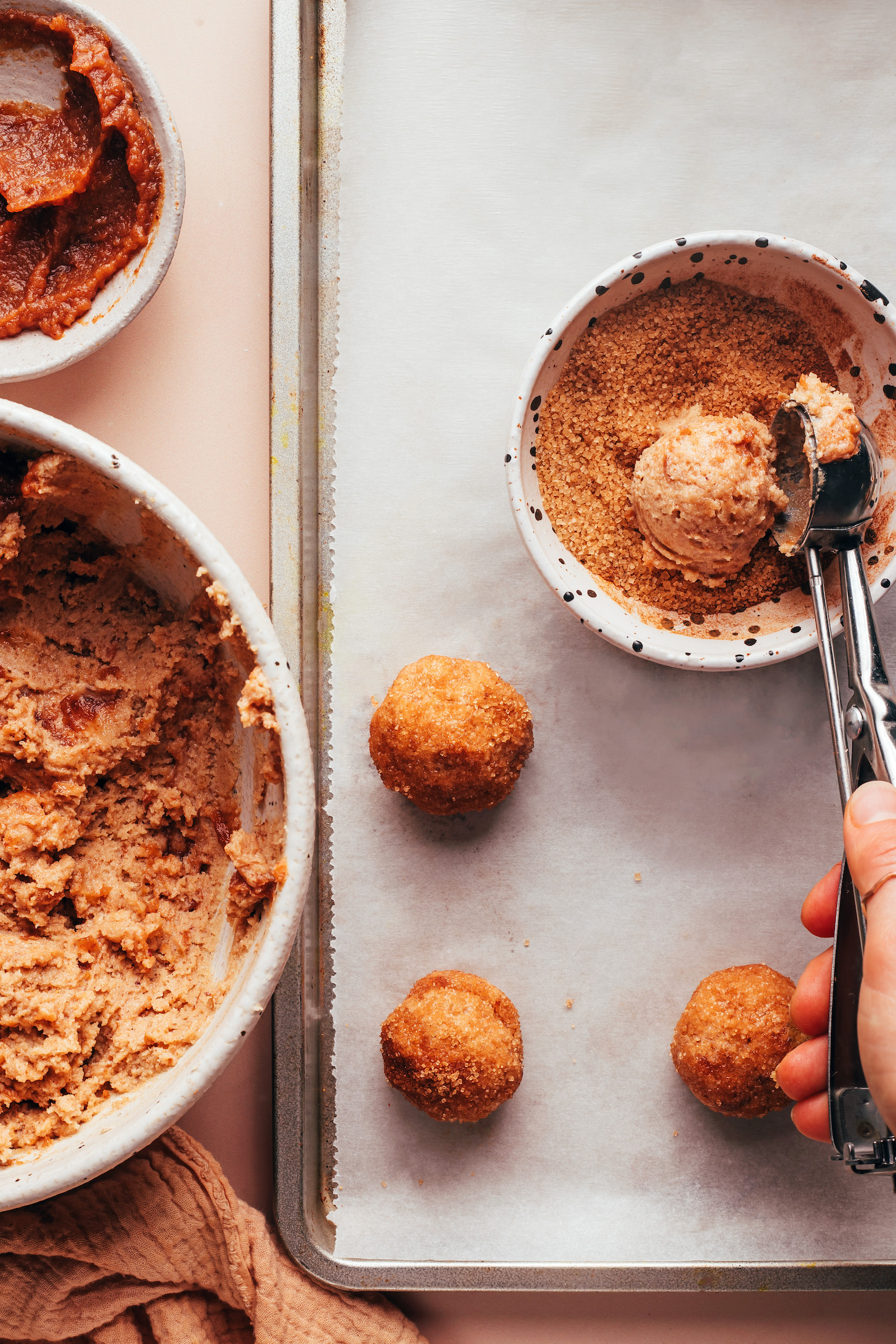 Using a cookie scoop to add apple butter snickerdoodle cookie dough to a bowl of cinnamon sugar